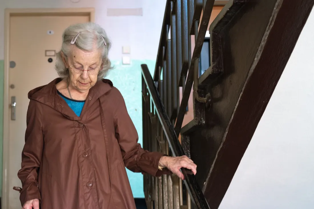 Femme âgée qui descend l'escalier de son immeuble en tenant la rampe